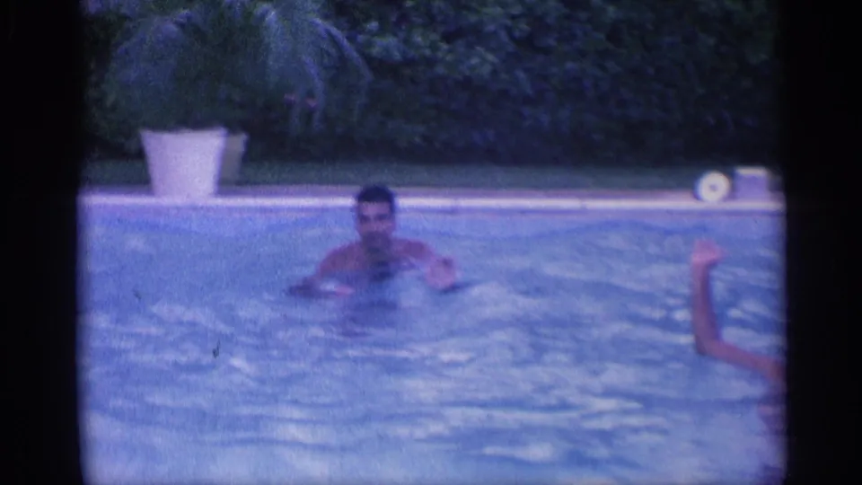 1959 Indiana 8mm frame showing a swimmer in blue pool water, with a second person partly visible at the edge.