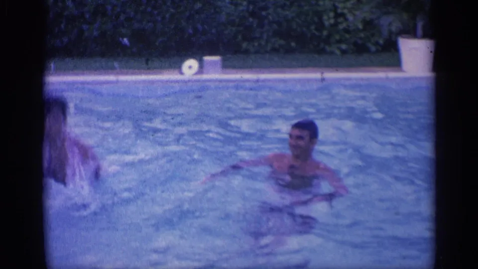 1959 Indiana home-movie frame of a swimmer in a backyard pool, with another swimmer partly visible at the left edge.