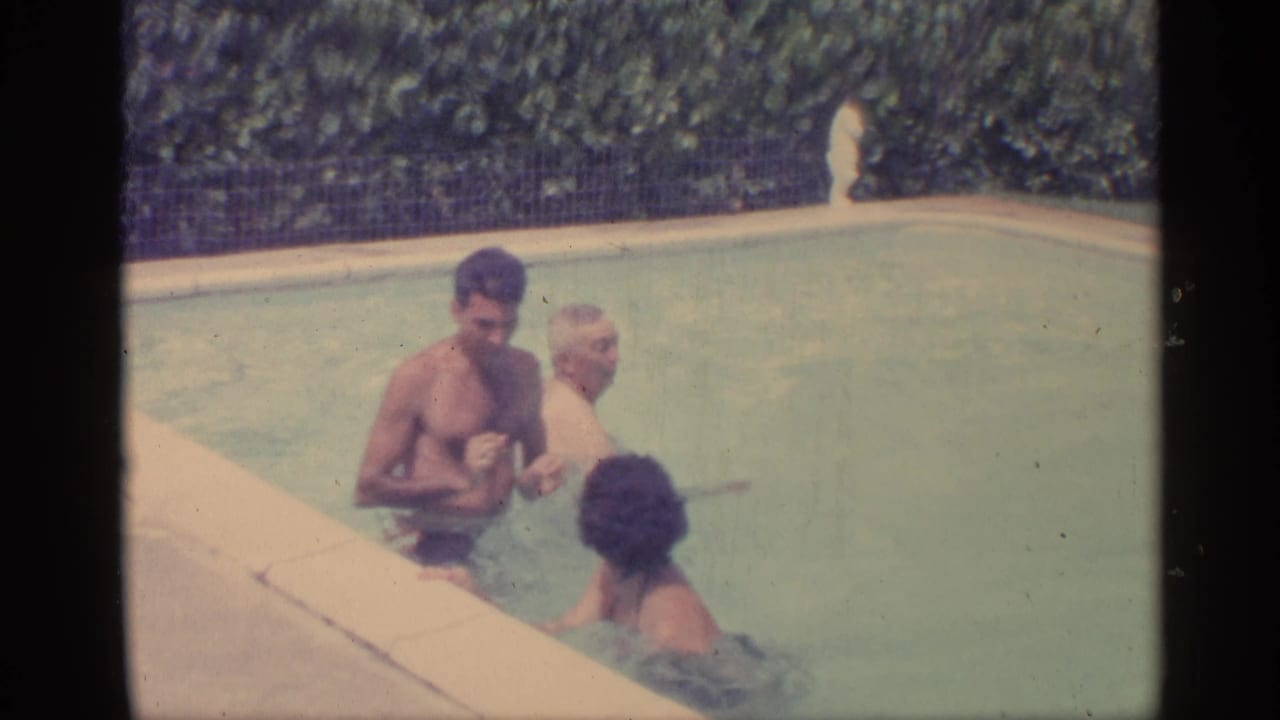 Adults stand in a backyard pool while one person faces the camera area.