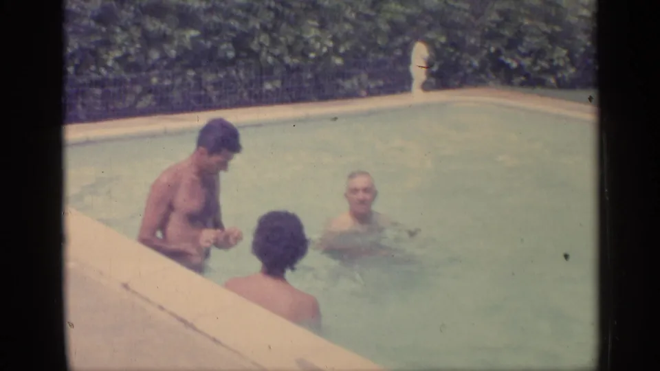 Indiana 1959 8mm frame showing adults in a backyard pool, with one person turned away and another facing forward.