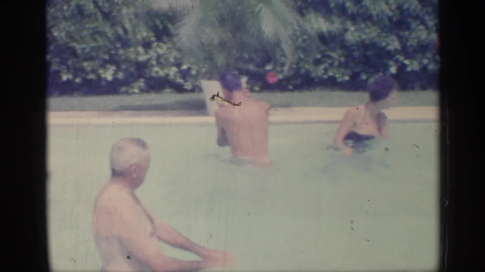 1959 Indiana home-movie frame showing three family members in a backyard swimming pool with hedges behind them.