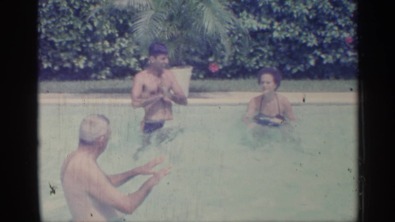 Three people standing in a swimming pool with foliage and a potted palm behind them.