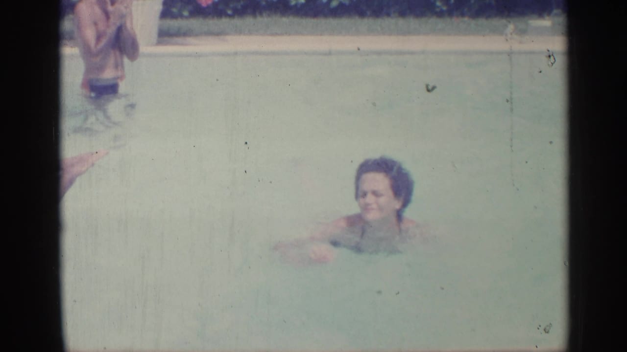 A woman swims in pale pool water while another person is partly visible near the top edge.
