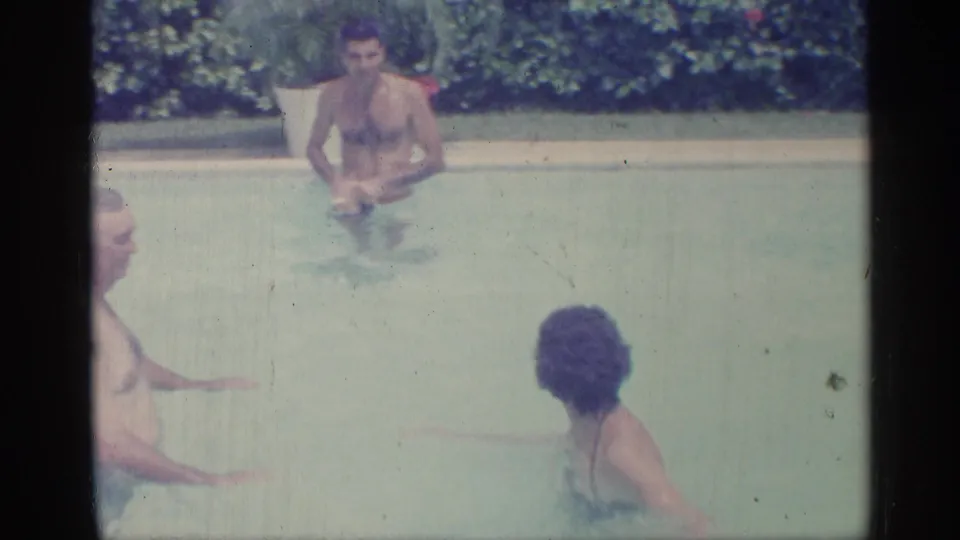 1959 Indiana 8mm frame showing swimmers gathered in an outdoor pool, including a man centered near the far side.