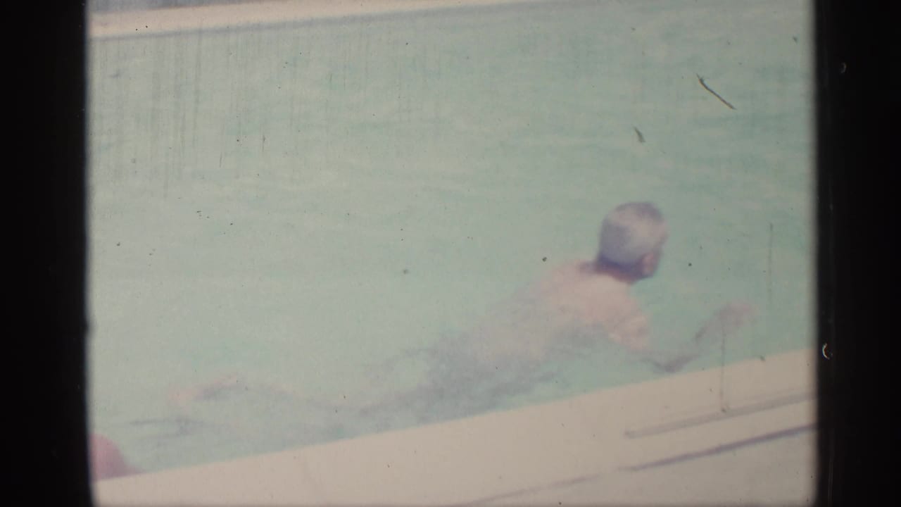 Adult swimmer seen near the pool edge in softly faded color footage.