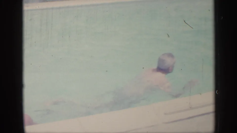 1959 Indiana home-movie frame with an adult swimming close to the edge of a backyard pool.