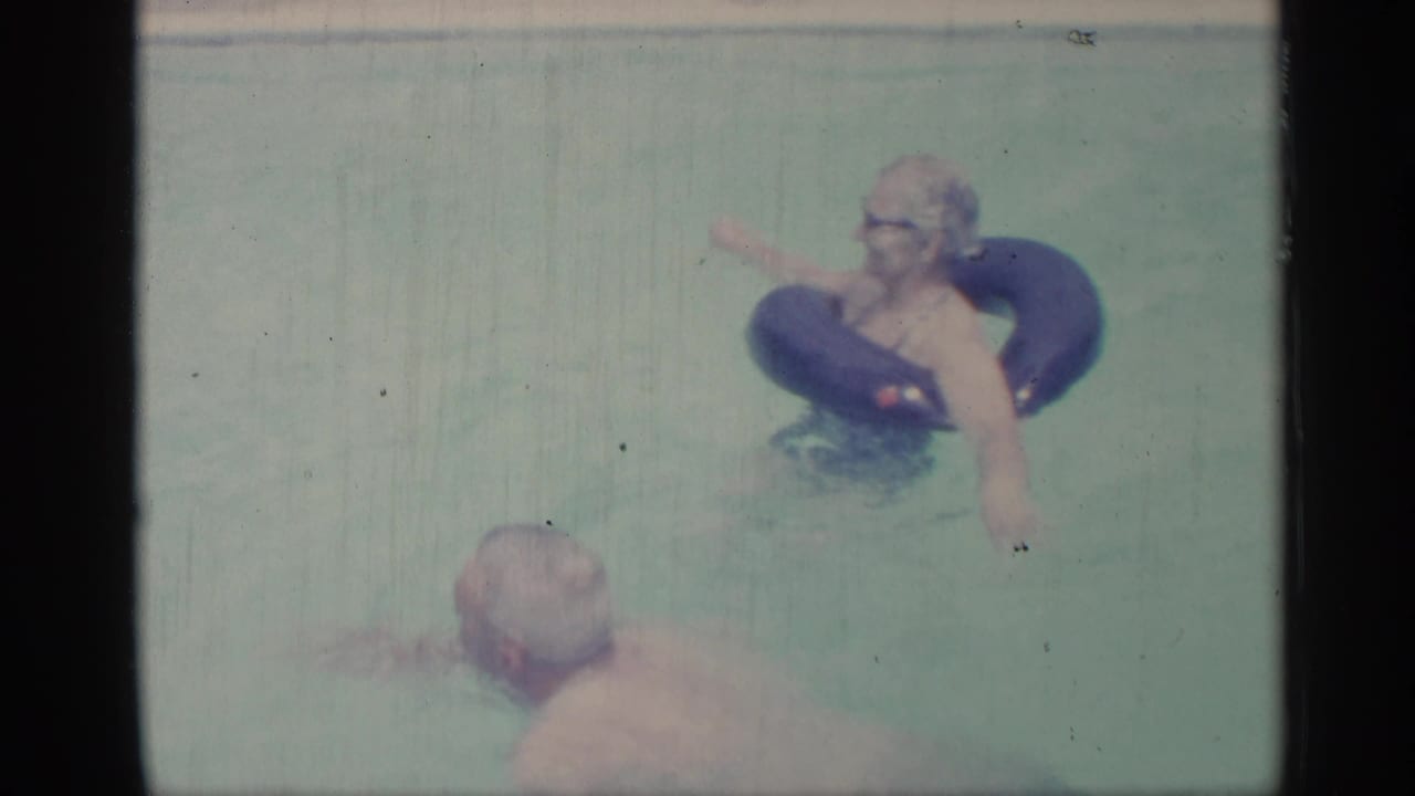 Woman floating on a blue inner tube while an adult man swims in a pool.