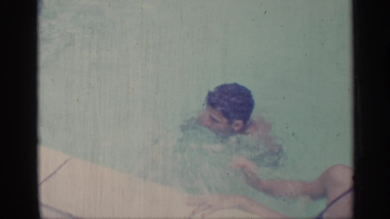 Young man treads water beside the pool edge with ripples around him.