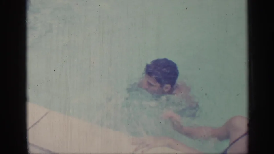 A young man with wet dark hair treads water in a backyard pool, filmed in 1959 Indiana home-movie footage.