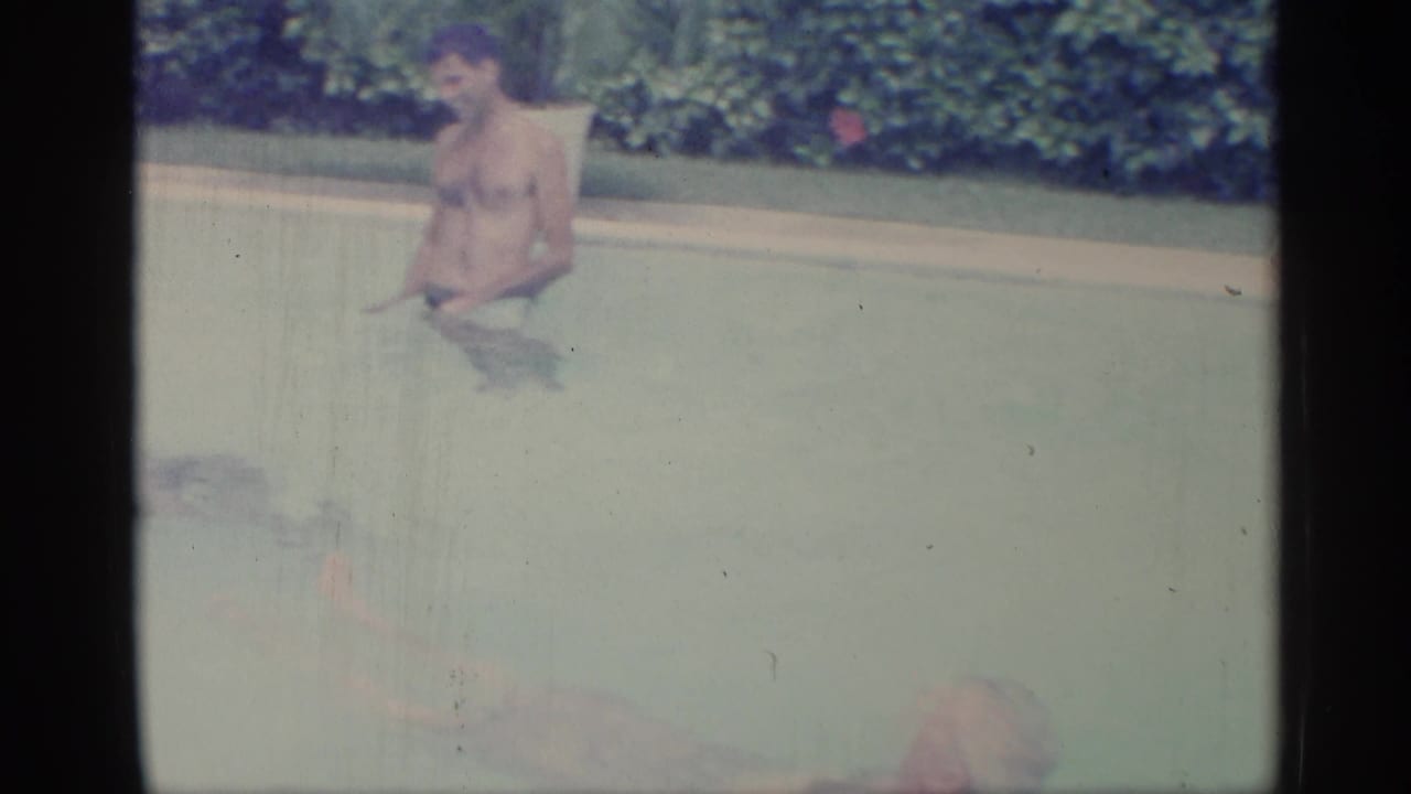 Adult man standing in a swimming pool with hedges behind him.