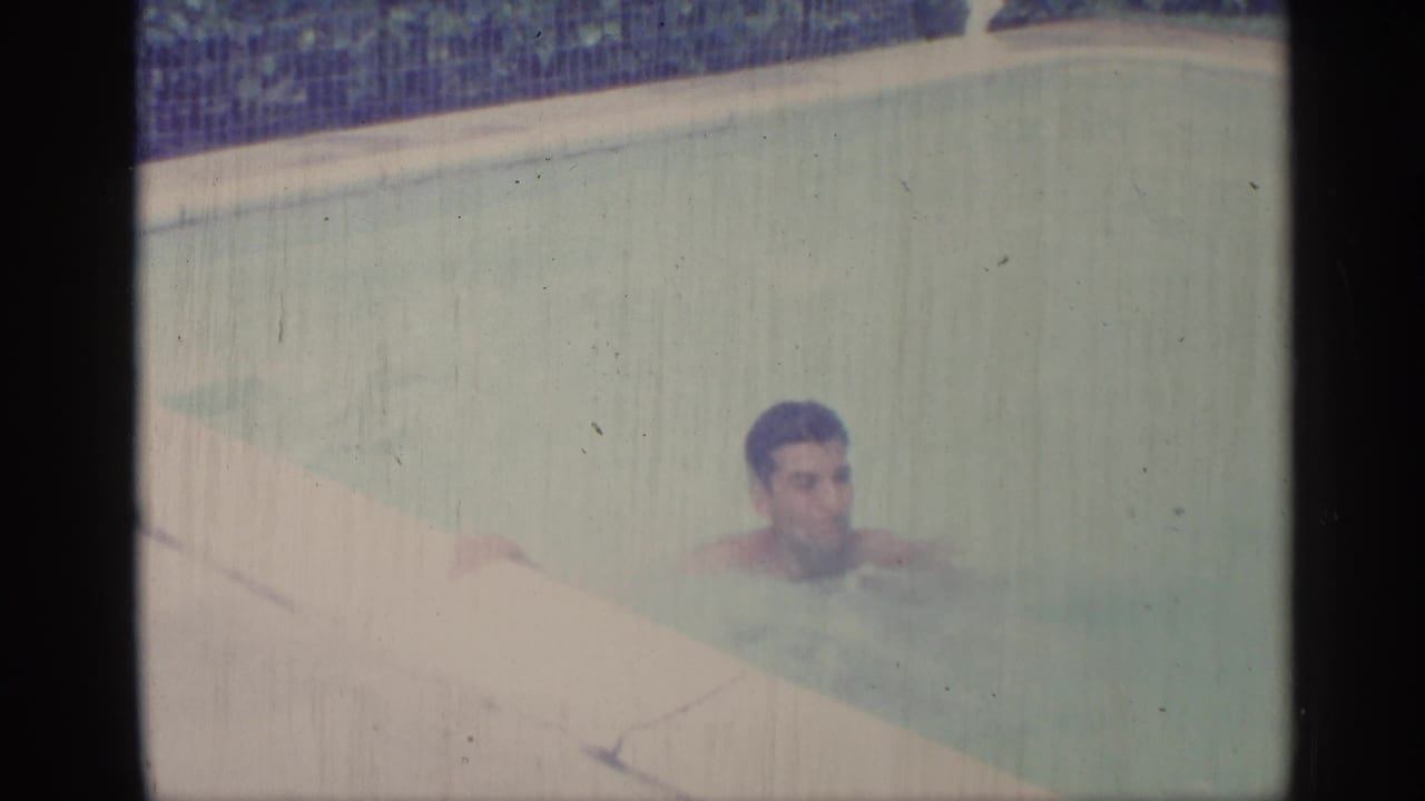 Adult man swimming near the edge of a pale blue pool.