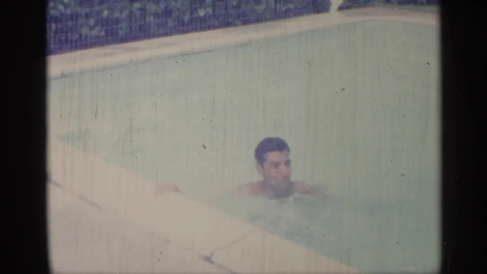 An adult man swims close to the pool coping in a faded 1959 Indiana home-movie frame.