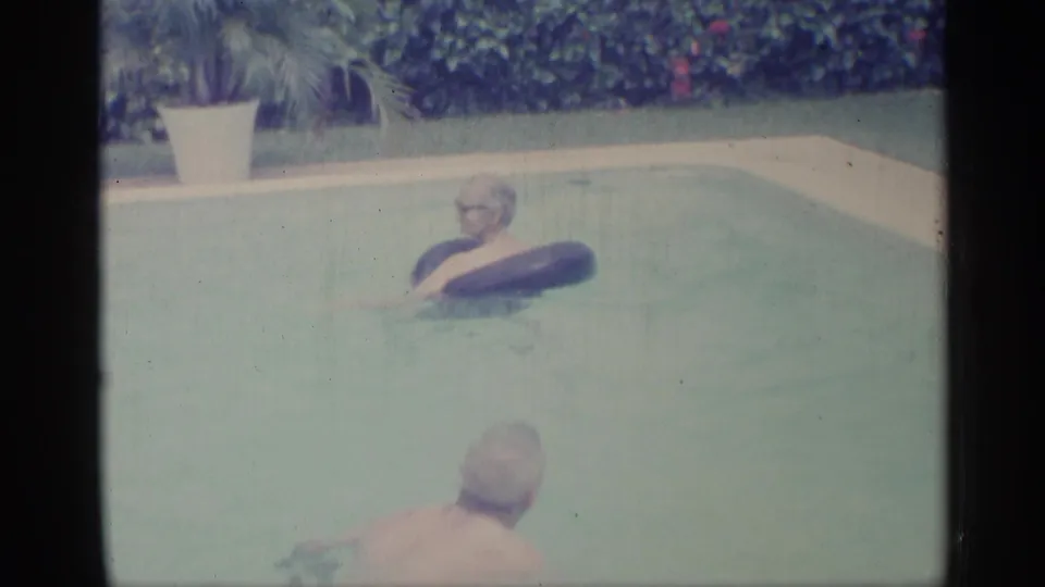Adult swimmers share a pool in Indiana 1959 footage, with one man using a dark inner tube near the far side.