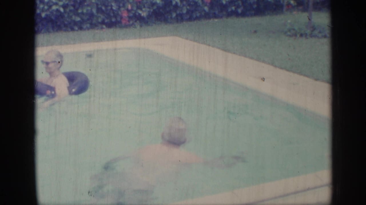 1959 Indiana pool scene with a person in glasses holding a dark inner tube and a second swimmer moving through the water.