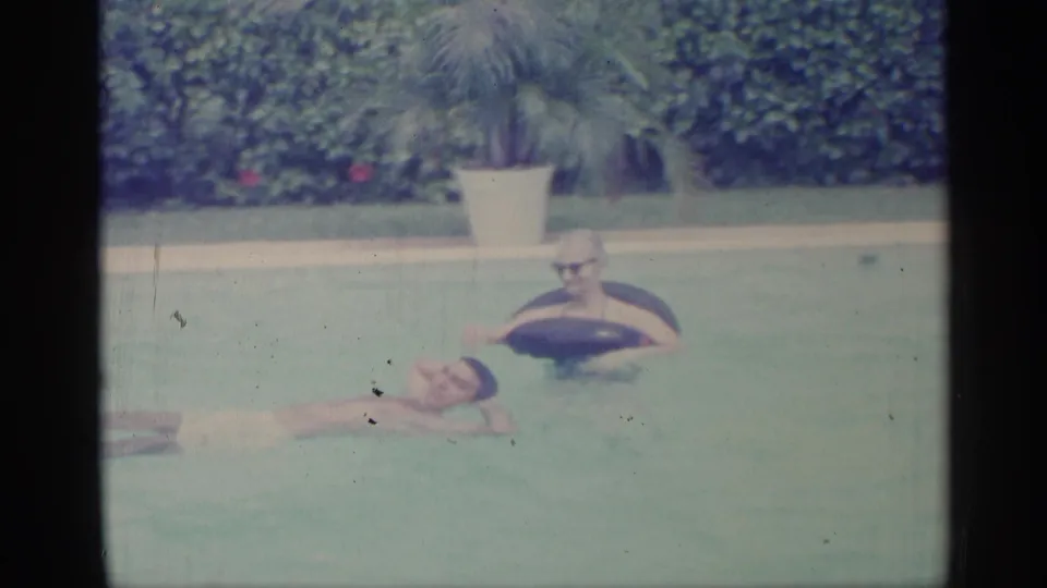 1959 Indiana backyard pool frame with one swimmer floating on their back and another person in glasses resting in a dark inner tube.