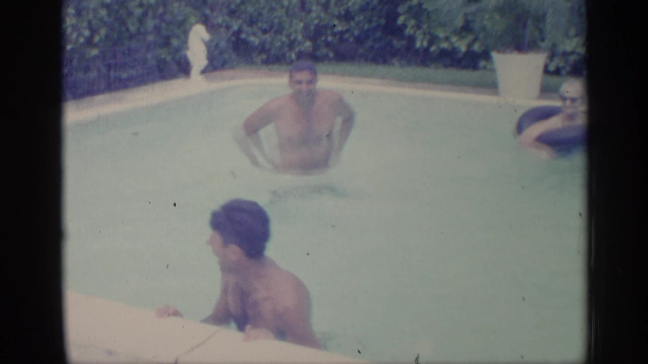 Men in a backyard swimming pool with hedges and a potted plant behind them.