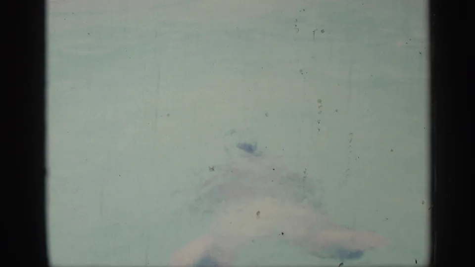 An adult swimmer is partly submerged in the pool, seen through faded 8mm color and soft motion blur.