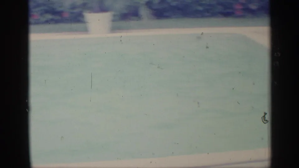 A brief 8mm frame shows the pale water and edge of the backyard swimming pool, with the swimmer out of view.