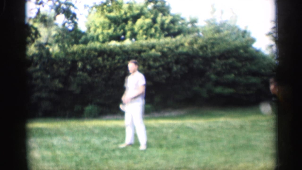 Man in white pants stands on grass holding a croquet mallet near hedges.
