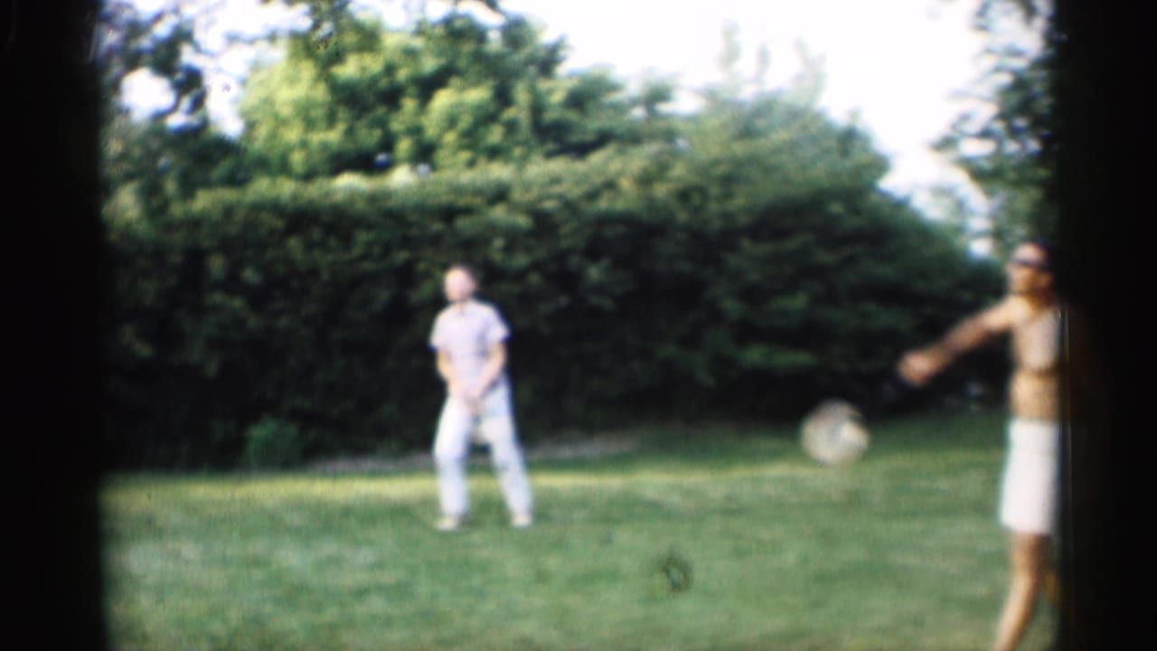 Two men play badminton on a green backyard lawn near hedges.