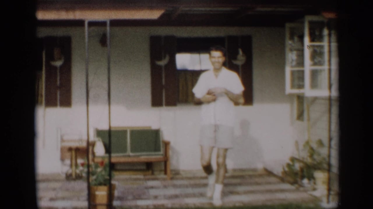 A young man in a white shirt and shorts smiles while approaching the camera on the porch of an Indiana home.