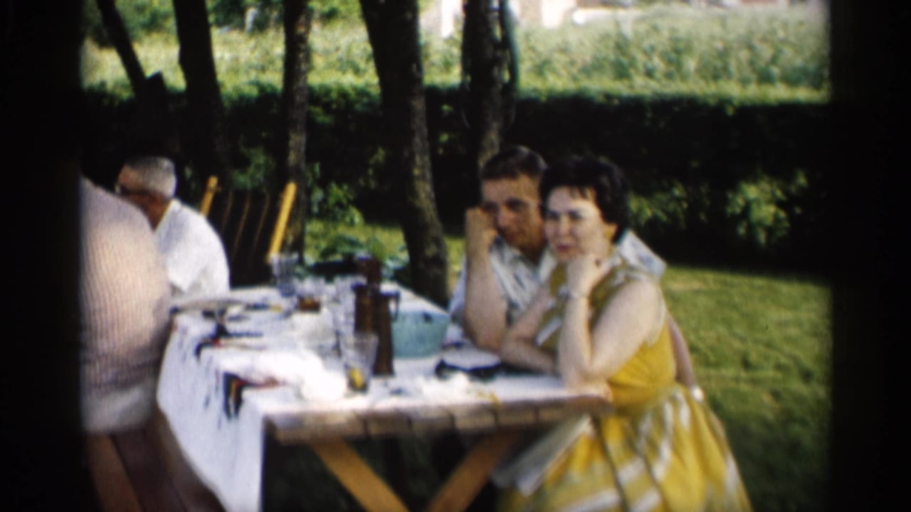 Woman in a yellow dress and man seated at an outdoor picnic table.