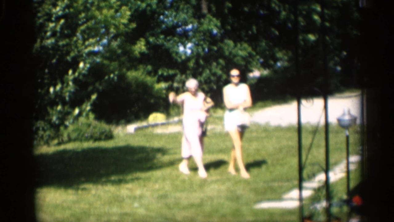 Two women walk across a sunny lawn toward a house.