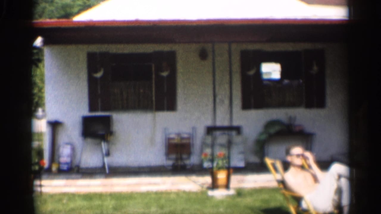 Man reclines in a lounge chair on a backyard lawn beside a white house.