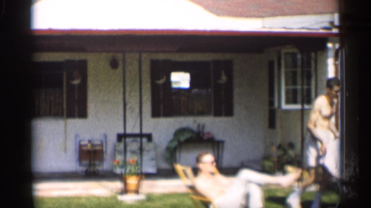 A reclining man sits near the house while another adult stands at the edge of frame.