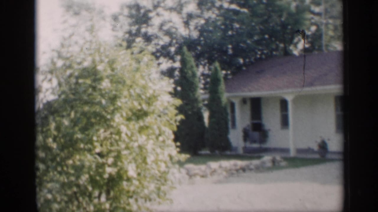 White single-story ranch house seen through trees with a covered porch and lawn.