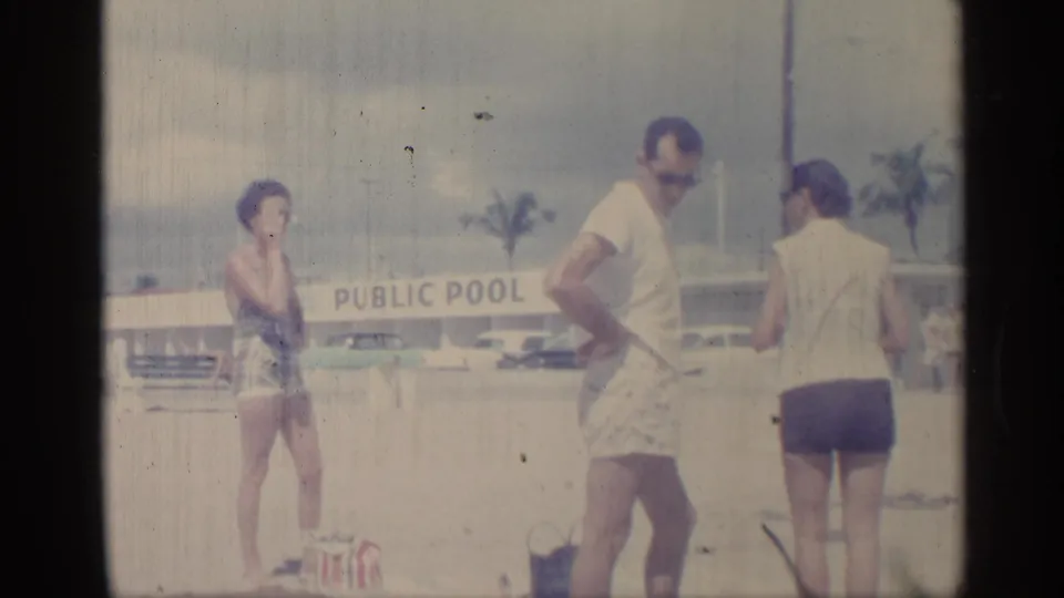 1959 Indiana frame showing adults in swimwear near the sandy poolside, with the PUBLIC POOL sign and parked cars behind them.