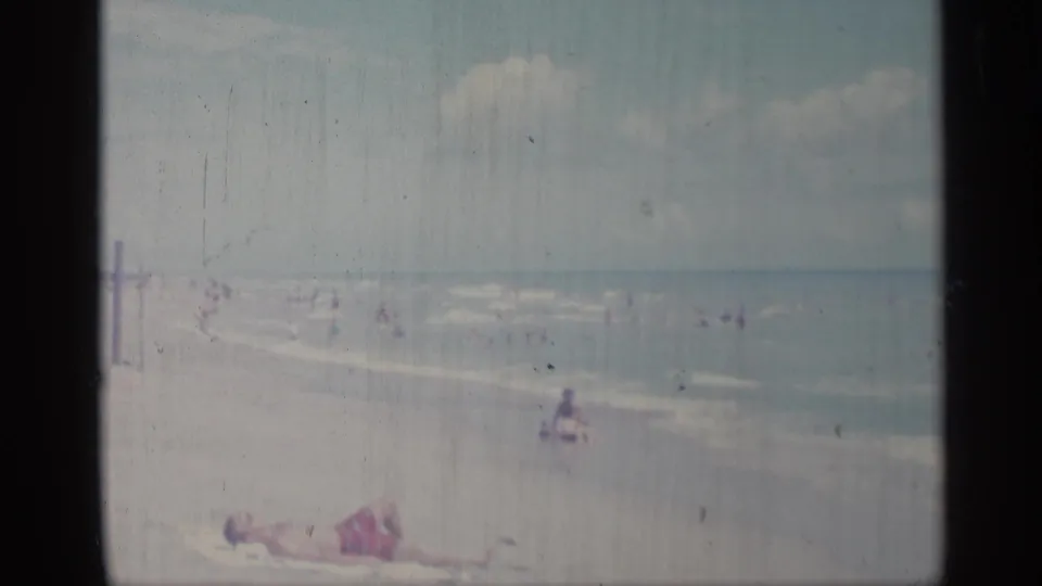 A 1959 Indiana beach view shows people swimming near the surf while a sunbather lies on the sand under a partly cloudy sky.