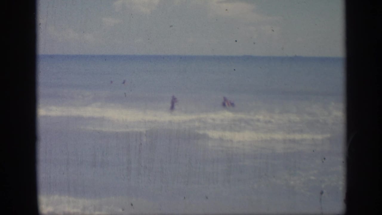 Distant swimmers stand and wade in ocean surf under a hazy sky.