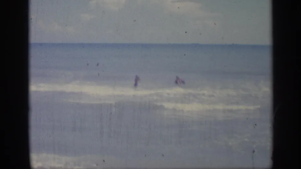 Supported by the clip metadata, this 1959 Indiana beach frame shows distant people wading in surf with soft 8mm color and gate edges.