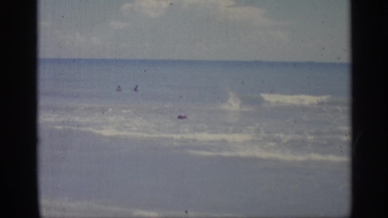 Ocean surf with several distant figures and a breaking wave offshore.