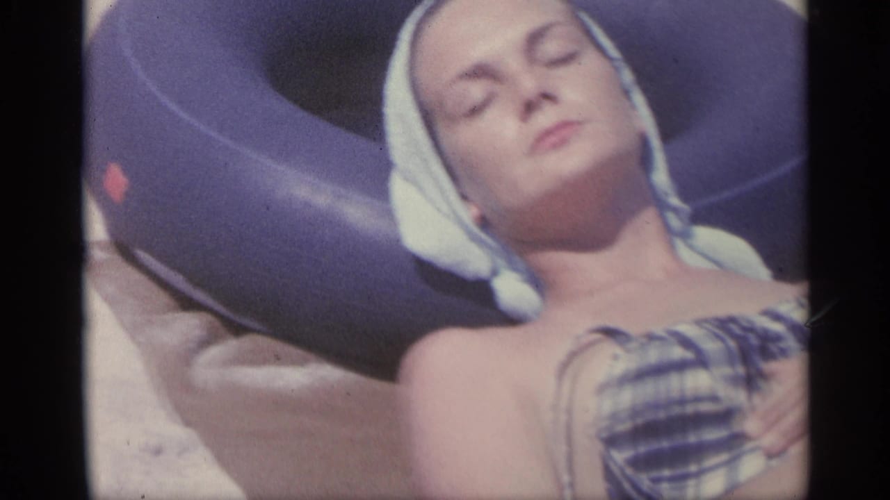 Woman in a plaid swimsuit rests on sand with a towel around her head.