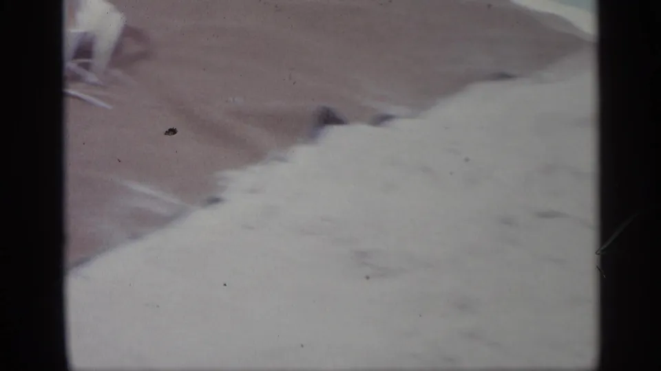 1959 Indiana 8mm frame showing a close cropped person reclining on a striped towel, with soft focus and pale fabric across the lower frame.