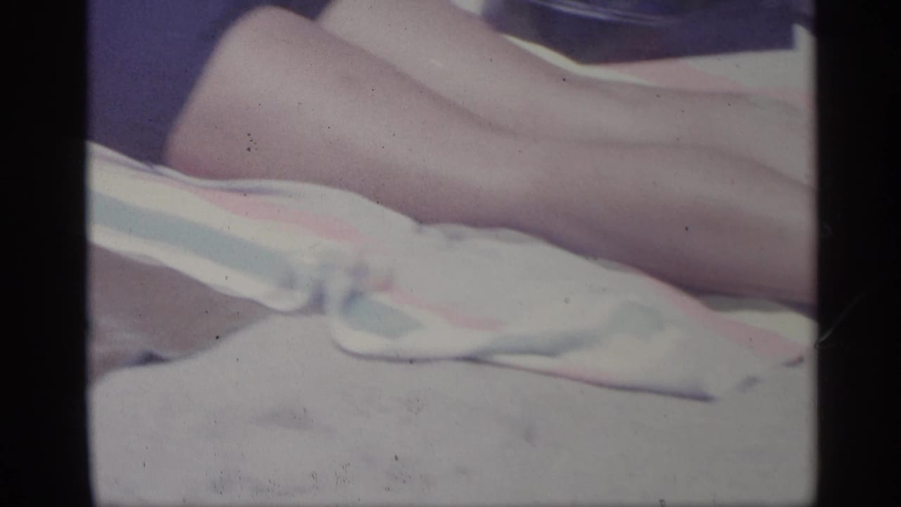 Bare legs and a white cloth are visible on a striped beach towel.