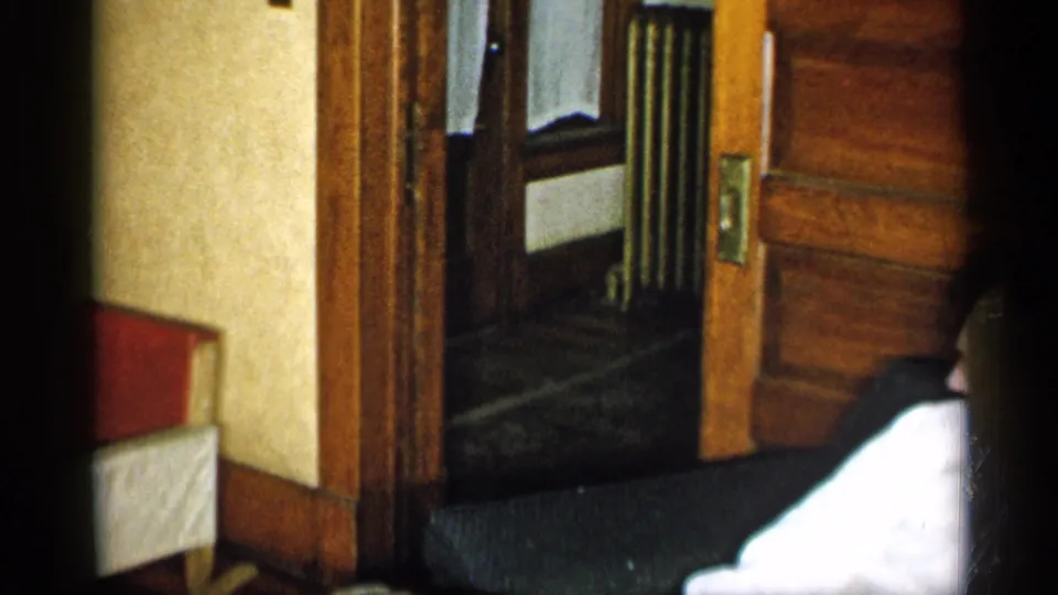 The final frame crops the seated man at the right edge while emphasizing the wood doorway, wall surfaces, and dark couch in the room.
