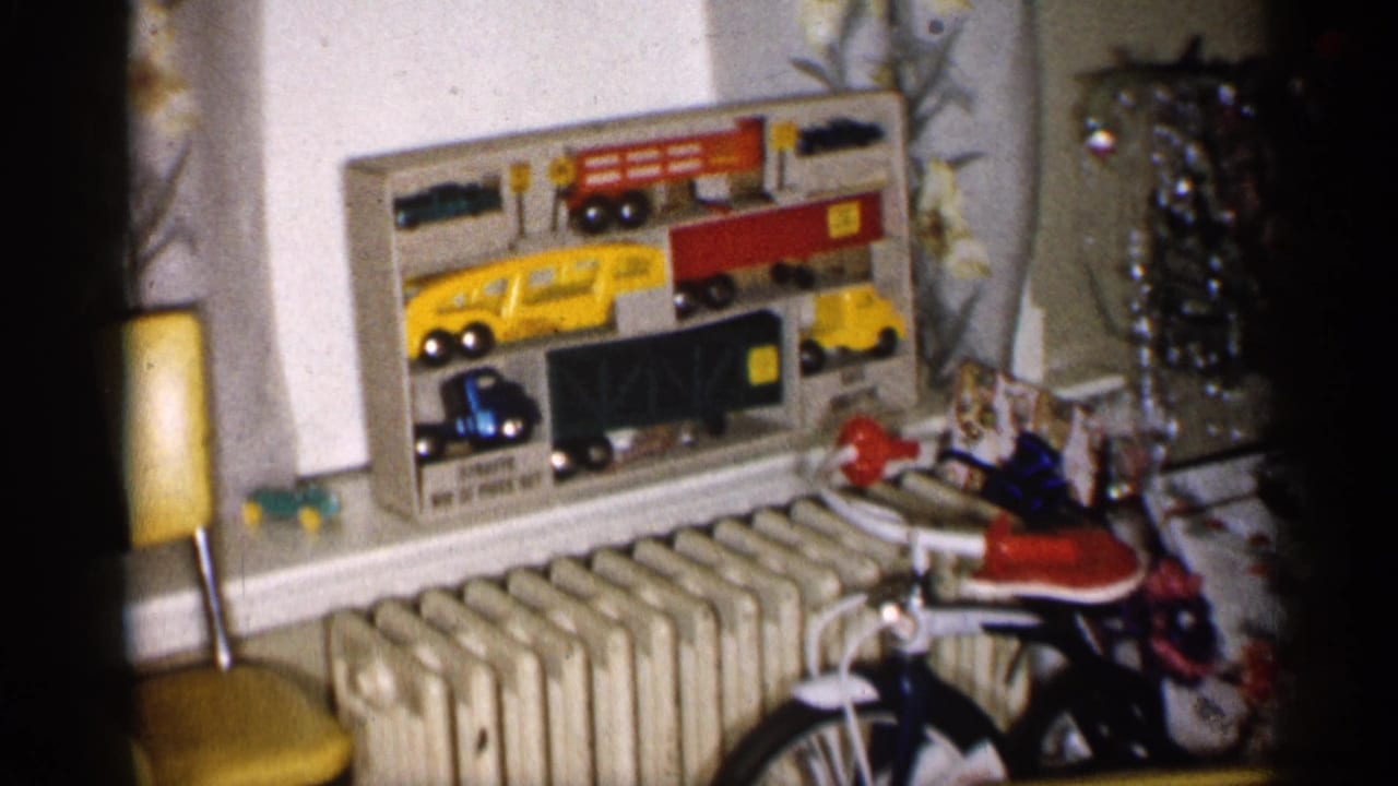 1959 Michigan home-movie frame showing a toy vehicle set, small children's bicycle, radiator, yellow chair, and Christmas tree in a private interior.
