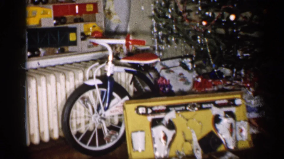 1959 Michigan frame showing a child-size bicycle near a decorated Christmas tree, boxed toy set, radiator, and wrapped gifts in a home.