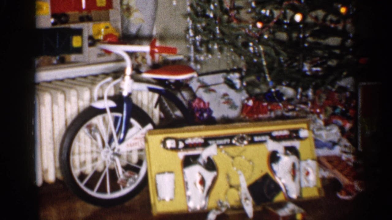 1959 Michigan 8mm frame showing a child-size bicycle, boxed toys, tinsel, and wrapped gifts beneath a Christmas tree.