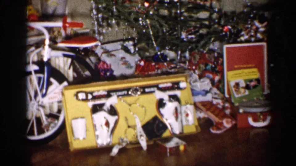 1959 Michigan 8mm frame with a large yellow toy box, bicycle wheel, wrapped gifts, tinsel, and a red-and-yellow display box near the tree.