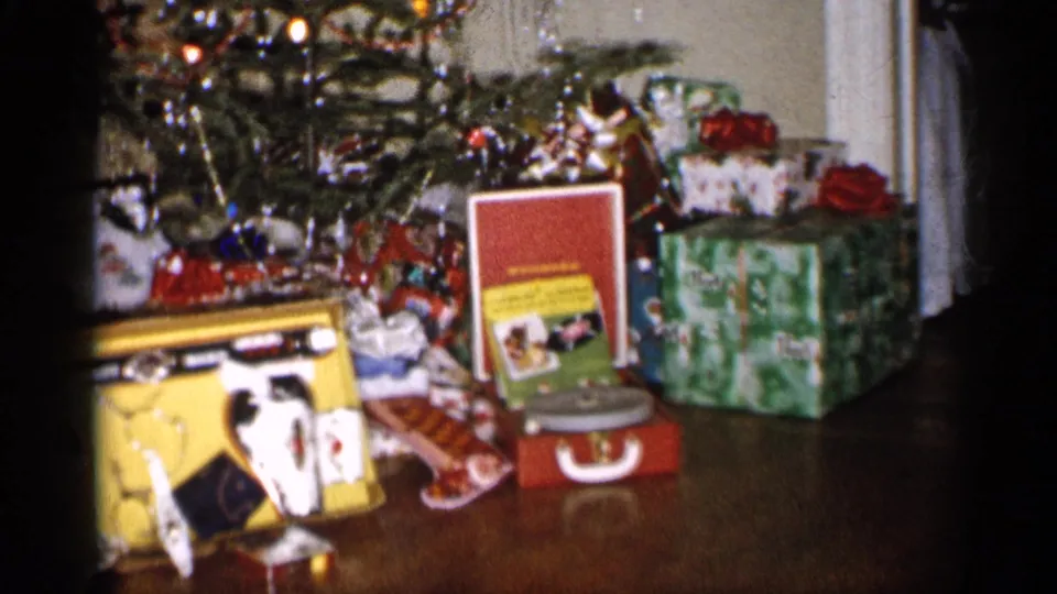 1959 Michigan home-movie frame of wrapped Christmas gifts and toys placed under a tinsel-decorated tree.
