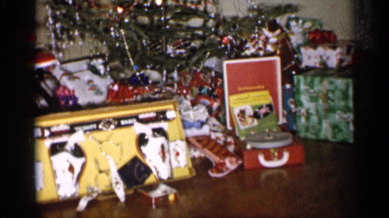 Christmas gifts and toys arranged beside a decorated tree on a wooden floor.