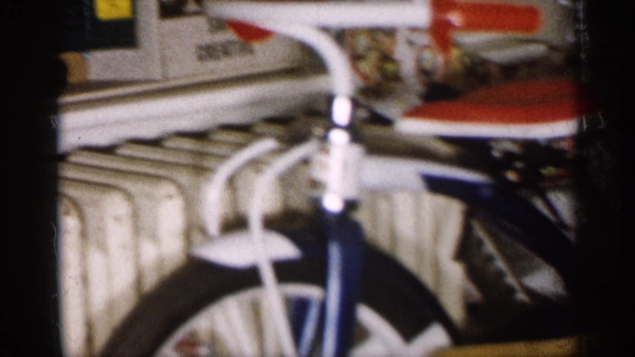 1959 Michigan home-movie frame with a child's bicycle parts, radiator, and nearby toys in a crowded interior.