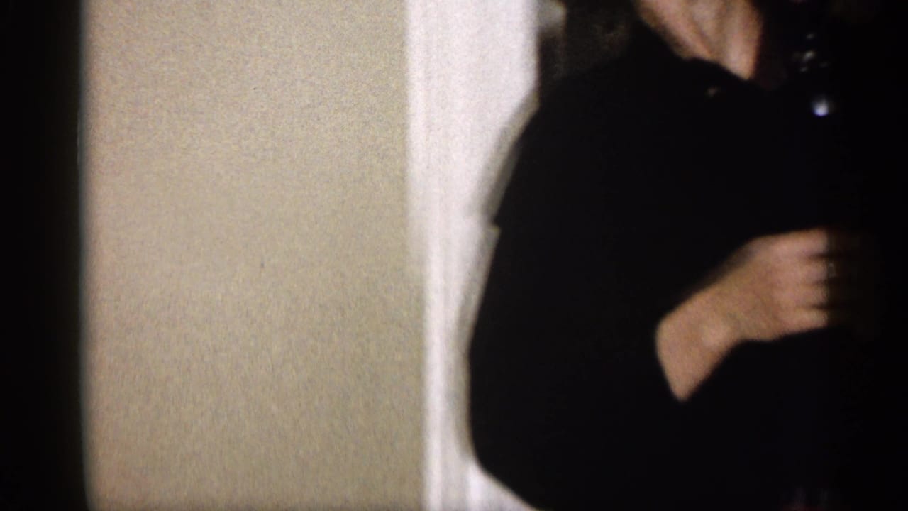 In a 1959 Michigan home interior, a woman in a dark dress stands partly cropped in a doorway near white trim.