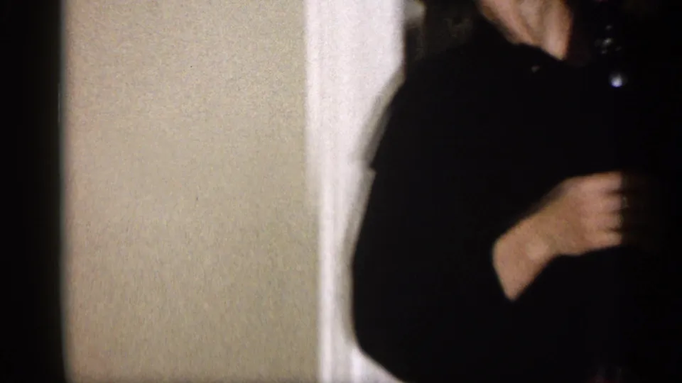 In a 1959 Michigan home interior, a woman in a dark dress stands partly cropped in a doorway near white trim.