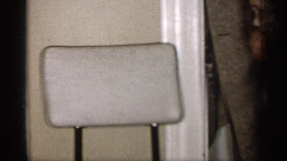A chair back sits against a plain wall while part of an adult figure appears at the right edge of the home interior.