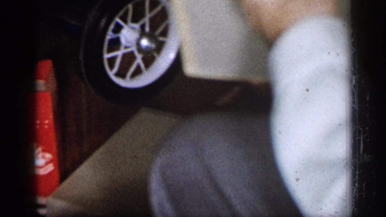 Close 1959 Michigan home-movie view of a white-spoked toy wheel and red bicycle part beside a seated person.